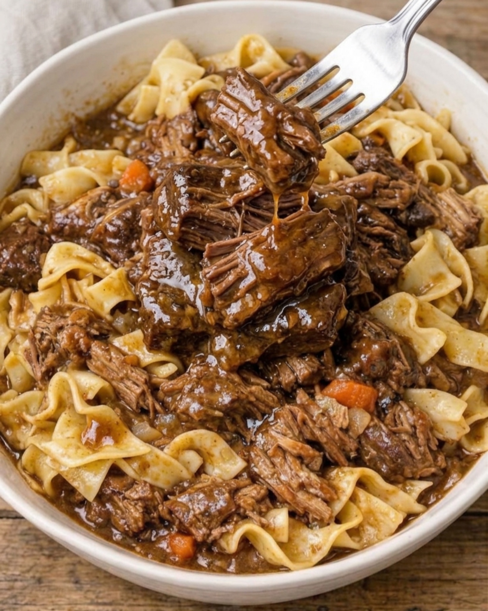 close-up of slow cooker beef and noodles with tender shredded beef, thick brown gravy and a fork lifting a piece